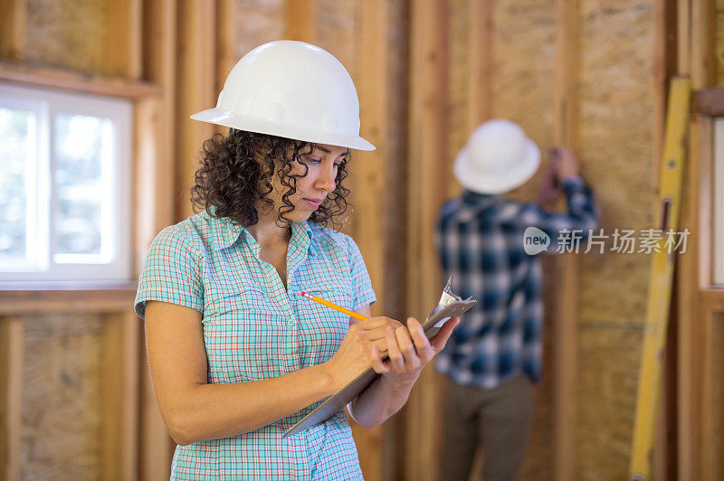 一位女建筑工人在一个剪贴板上计划建筑项目的下一个阶段