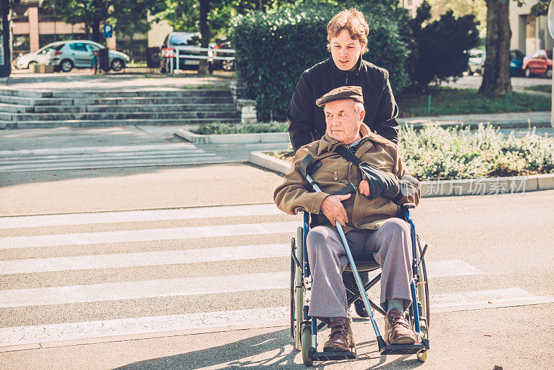 坐在轮椅上的老人和孙子穿过街道，欧洲