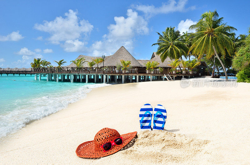 戴着太阳帽、戴着太阳镜、穿着拖鞋在热带海滩上