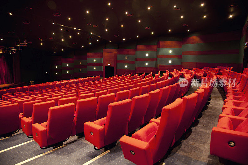 一个空的低灯光的剧院，有一排排的红色座位