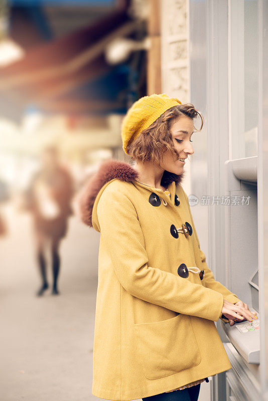 一个年轻女子在街上的自动取款机旁。
