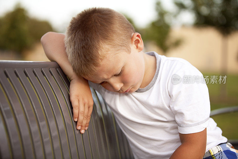 悲伤的小男孩独自坐在长凳上，头朝下