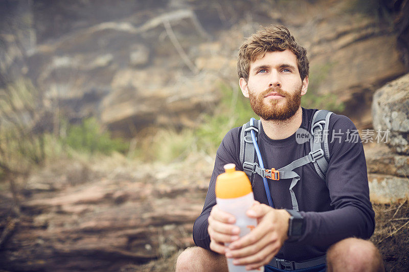 有思想的徒步旅行者拿着水瓶坐在岩石上