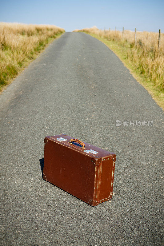 空无一人的乡村路上，一只破旧的手提箱。
