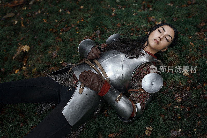 一个美丽的女战士穿着链甲和盔甲躺在一个神秘的森林里。