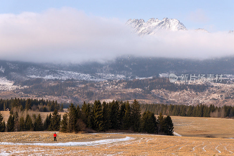 男人和山脉。一个穿红色夹克的男人在高塔特拉雪峰的背景下。Poprad山谷,斯洛伐克。《云中冬山》斯洛伐克冬季山地景观