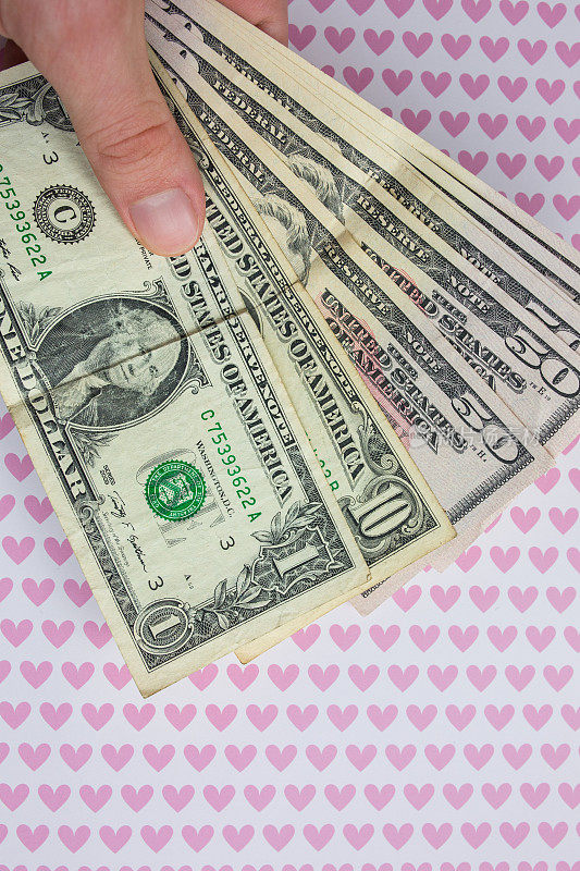 背景上的男人手里拿着钱，上面画着粉色的心。爱的美元。是时候去购物买东西了。钱购物狂上瘾。垂直的照片。
