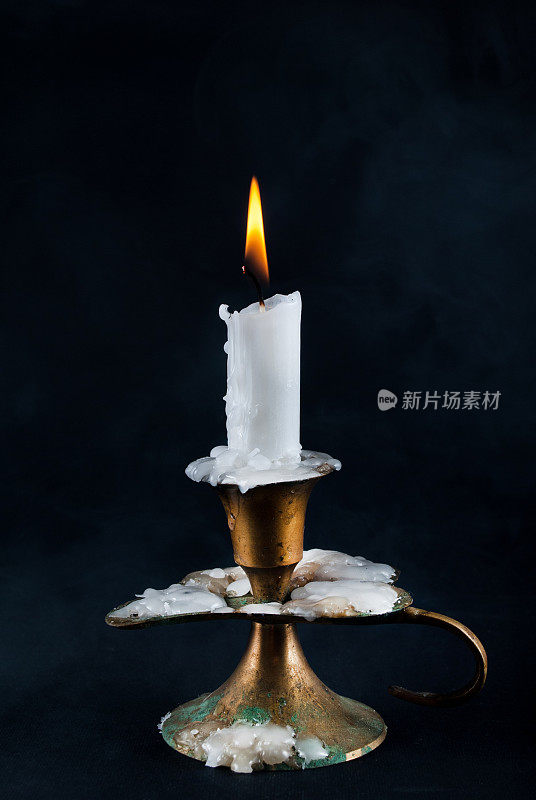 白色的蜡烛在旧烛台上燃烧，背景是烟