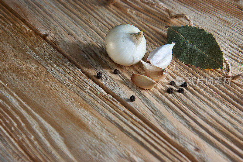木桌上放着洋葱、大蒜、黑胡椒和月桂叶