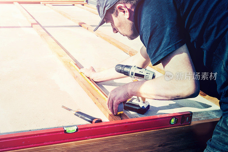 建筑工人用电瓶螺丝枪或电钻拧下木甲板。