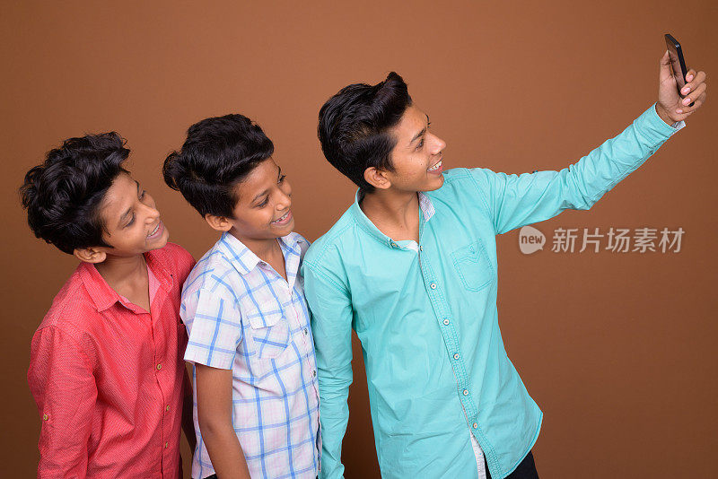 工作室拍摄的三个年轻的印度兄弟在拍视频，并在彩色背景下自拍