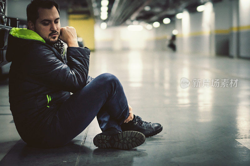 一个年轻人独自坐在停车场的地板上