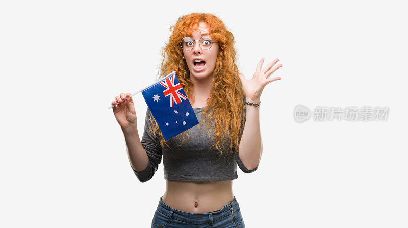 年轻的红头发妇女举着澳大利亚国旗非常高兴和兴奋，胜利者的表情庆祝胜利尖叫着大大的微笑和举手