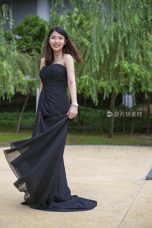 时尚的肖像年轻的亚洲妇女穿着美丽的正式长连衣裙站在外面的公园快乐