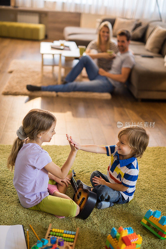 快乐的兄弟姐妹在家里的地毯上玩耍时互相击掌。