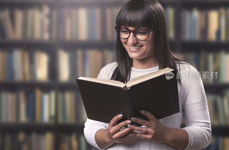 一个漂亮的微笑的女孩在图书馆看书的肖像