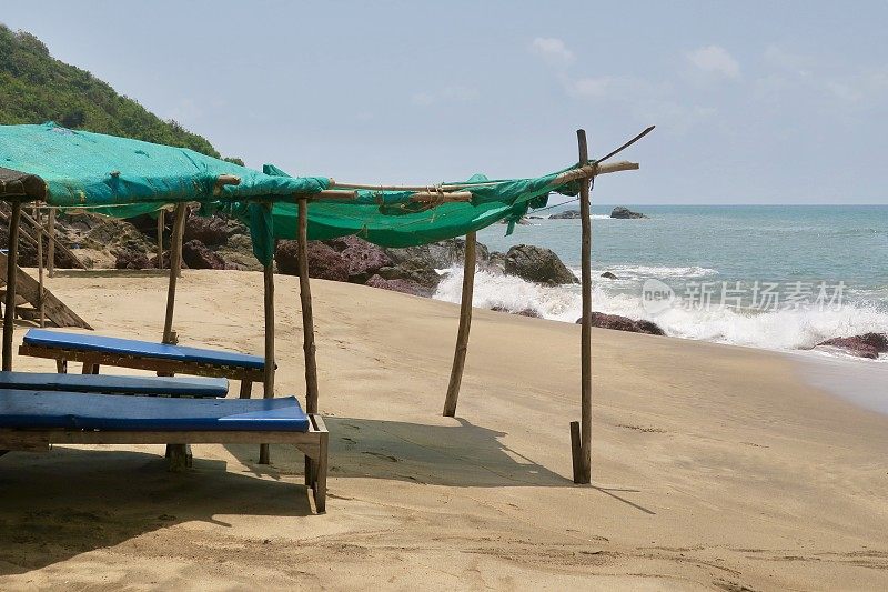 在印度果阿的可乐沙滩上，在水边的空旷的海边日光躺椅上，为保护阳光而建造的简陋遮阳棚