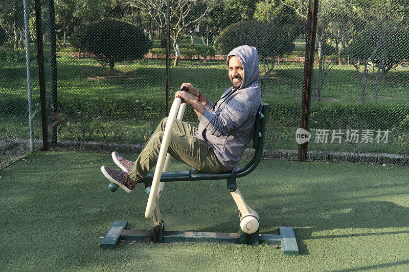 印度男子在户外健身房使用赛艇健身器材，在露天公园锻炼