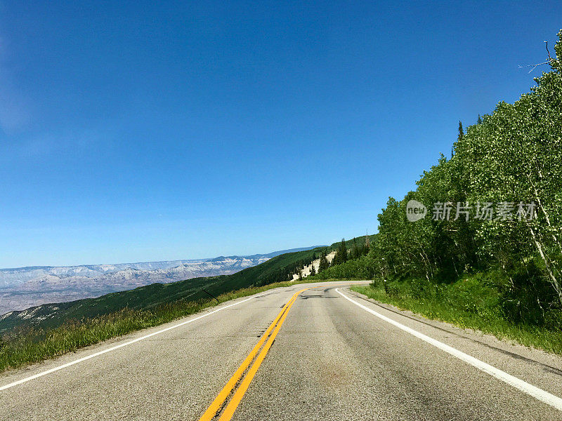 在一个晴朗的日子里，山上的高速公路两旁是绿色的树叶，蓝天白云