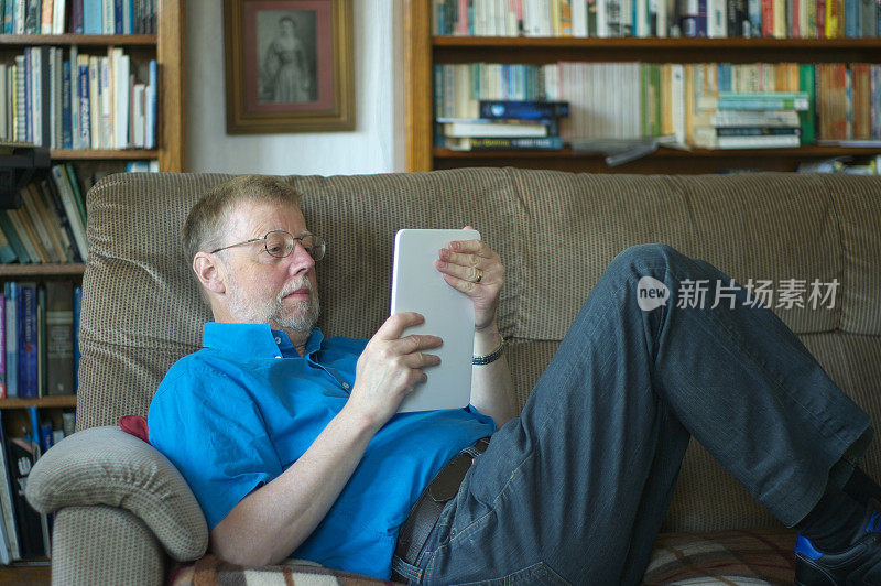 一名留着胡子的中年男子坐在沙发上用平板电脑放松