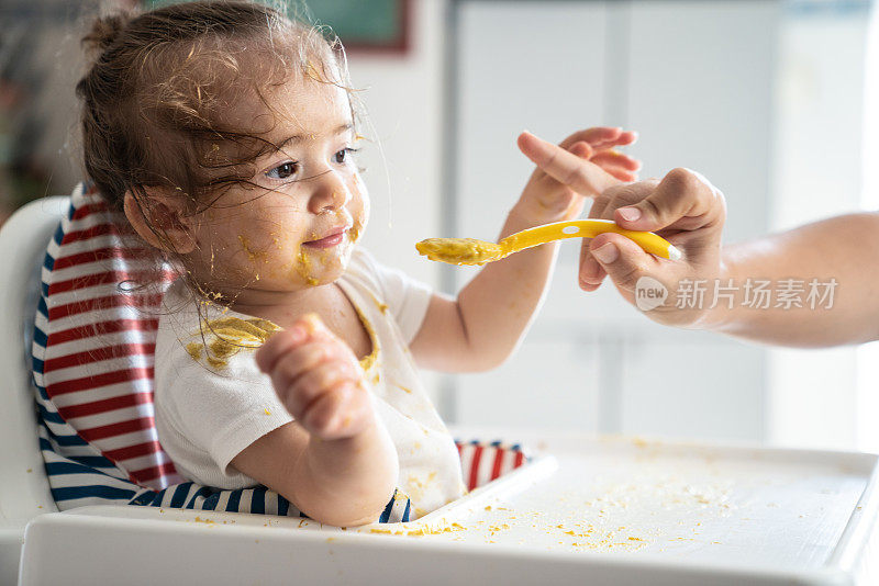 女婴坐在喂食椅上吃婴儿食品