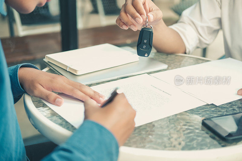 汽车经销商将钥匙交给车主。客户签署保险文件或汽车租赁表格