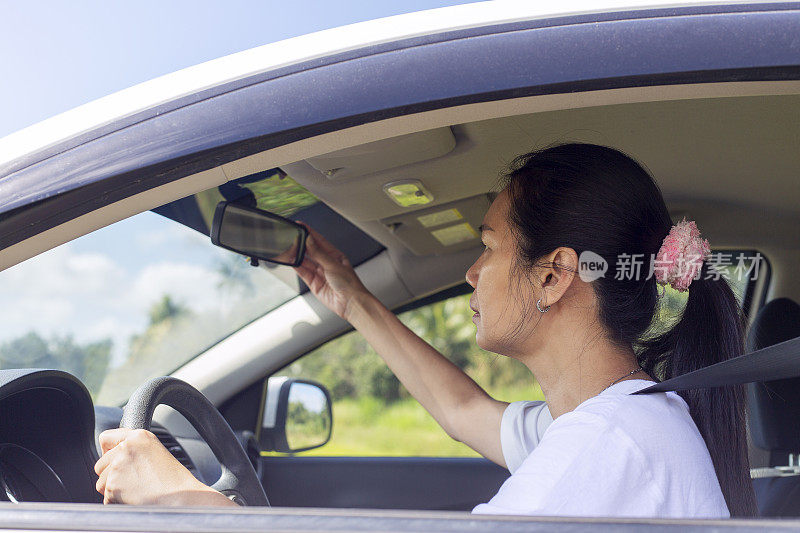 成熟的亚洲女性坐在汽车驾驶座上调整后视镜