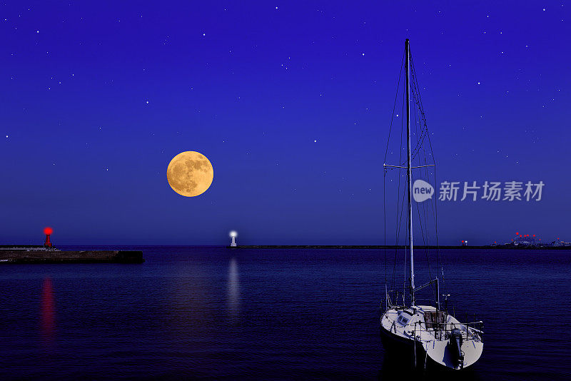 满月在游艇和灯塔上空升起。
