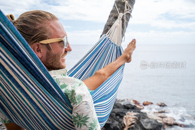 一名男子躺在挂在海滩棕榈树上的吊床上休息