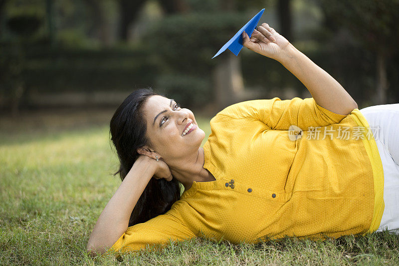 一个快乐的女人躺在公园的草地上扔纸飞机