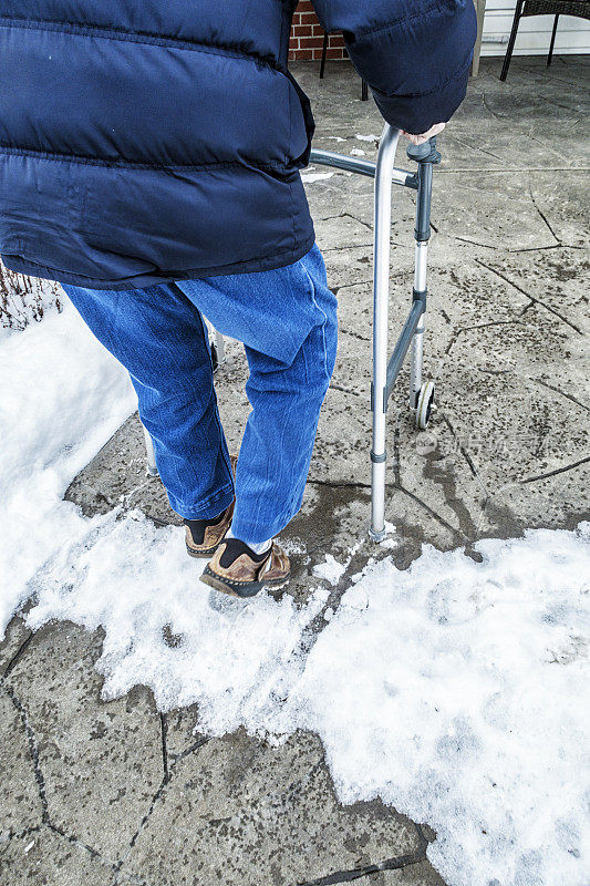 一位残疾老人在雪地里缓慢地推着移动步行者