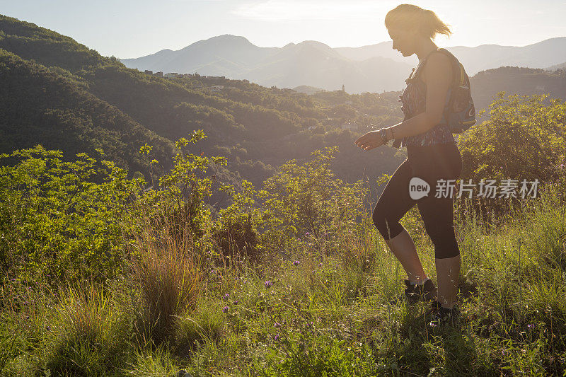 日出时，一名女性徒步旅行者穿过长满青草的山脊