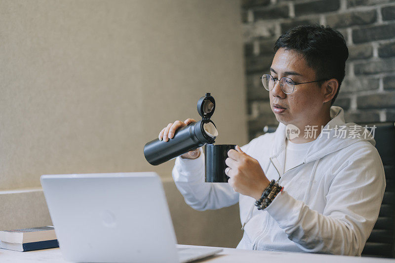 一位亚洲华人中年男子正在他的办公室喝咖啡休息