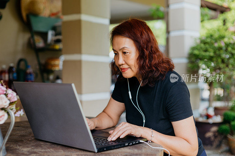 一位年长的亚洲女性在家里用笔记本电脑听音乐