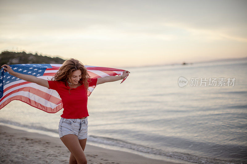 海滩上拿着美国国旗的年轻女子