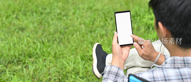 一名男子正坐在草地上使用一部白屏幕智能手机作为背景。