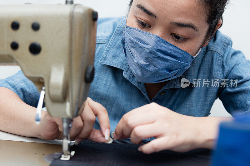 女裁缝企业家戴着防护面罩在她的工作室工作。大流行的生活方式的概念。