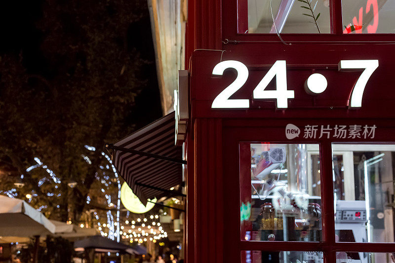 街角的红色店铺外立面有发光招牌，24小时24小时24小时，英式建筑风格的店铺配以玻璃橱窗，夜景是建筑和城市街道照明的细节。
