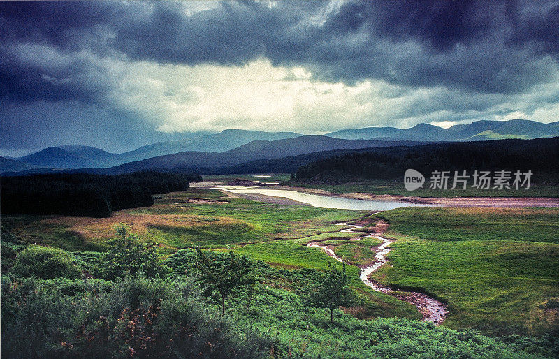 典型的苏格兰风景，湖泊和山脉。一场风暴威胁;乌云。在前景是一条小溪或小河。