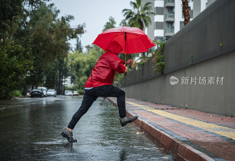 成熟的男人穿着红雨衣，撑着红伞走在雨中的城市街道上