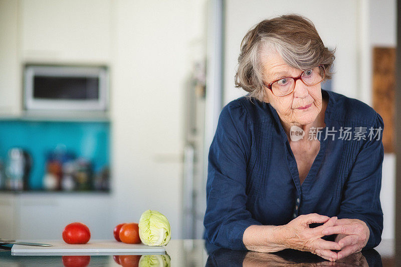 一位老妇人倚靠在厨房的柜台上，看起来困惑和心烦意乱