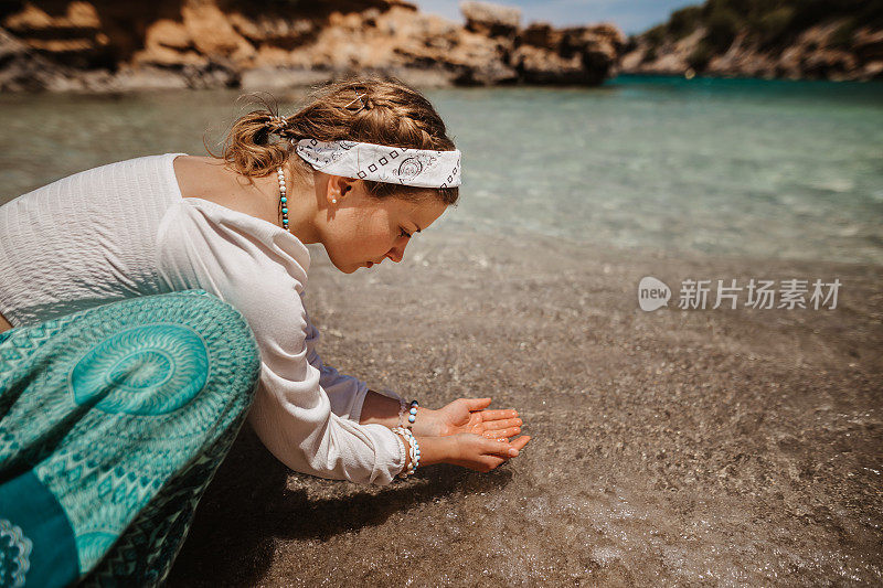 对自然充满热爱的灵性女人在阳光明媚的海滩上专注地握着水