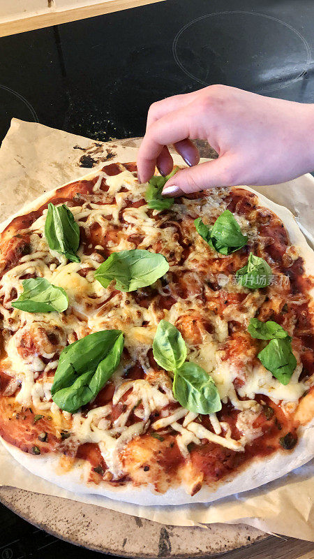 这是在厨房烤箱里自制的披萨，用披萨石做薄而脆的披萨底，意大利那不勒斯玛格丽塔披萨，磨碎的马苏里拉芝士，番茄酱，新鲜的罗勒叶洒在面熟的人手上