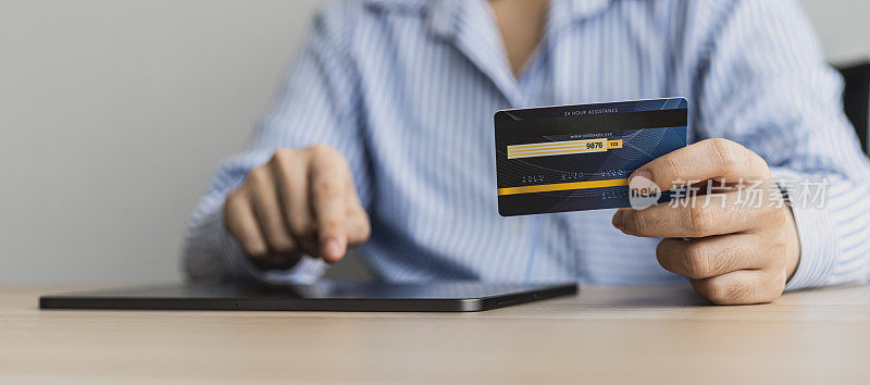 一位女士手持信用卡在平板电脑上打字，她在笔记本电脑上的购物应用程序中填写信用卡信息，为订单付款。使用信用卡支付的网上购物概念。