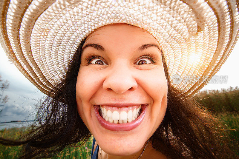 一个戴着帽子的女人的肖像特写，全脸，在广角镜头。扭曲的比例，滑稽的脸。迷人的微笑和完美的牙齿。