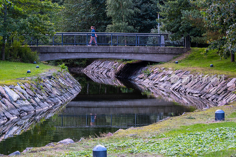 背景中有一座步行桥的小运河。一个男人和一个女人在夏日里散步。