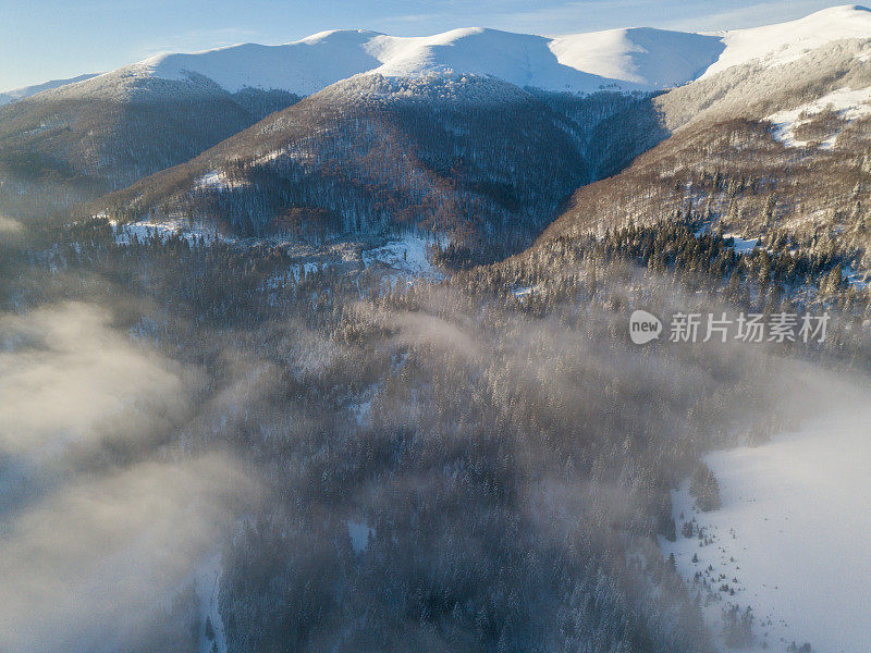 壮丽的日出在山上的空中拍摄。山与山之间的山谷被雾覆盖，被初升的太阳温暖的光线照亮。山上覆盖着天然的森林。