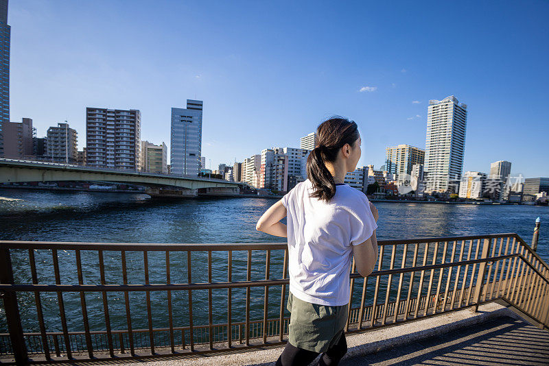 在城市的河边慢跑的女人的后视图