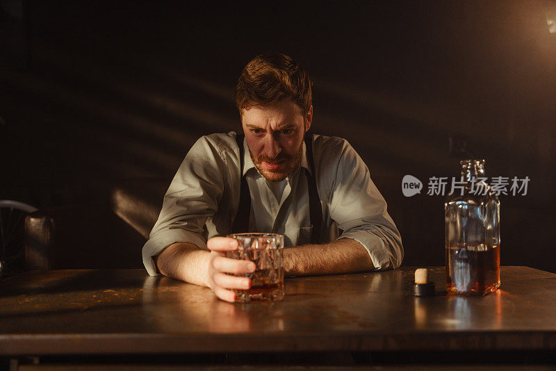 一幅气氛浓厚的肖像，一个孤独的醉汉在桌子上端着一杯威士忌。一个醉汉愤怒地看着手里的一杯威士忌。