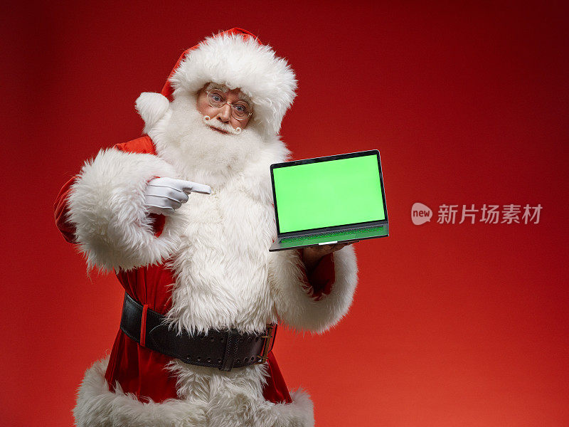 圣诞老人站在红色背景下，指着笔记本电脑屏幕上的Chroma键